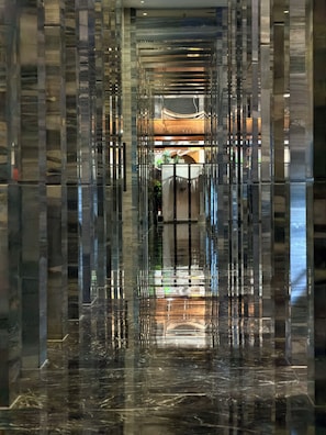 A corridor with reflective surfaces and a central area with a plant and a door. - Renaissance Guiyang Hotel (Guiyang)