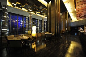 Un moderno vestíbulo de hotel con piso de madera oscura, mobiliario contemporáneo y un amplio ventanal con vistas a la ciudad de noche.