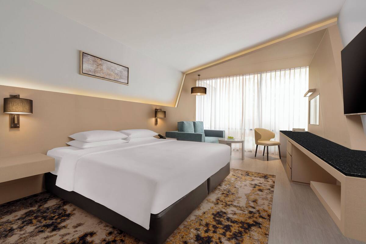 Una habitación de hotel moderna con una cama grande, un escritorio, una silla y un televisor.