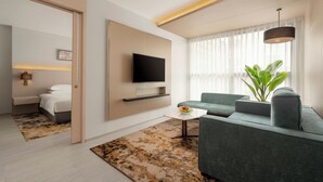 Une chambre d’hôtel moderne équipée d’un lit, d’une télévision, d’un canapé, d’une table basse et d’une plante.