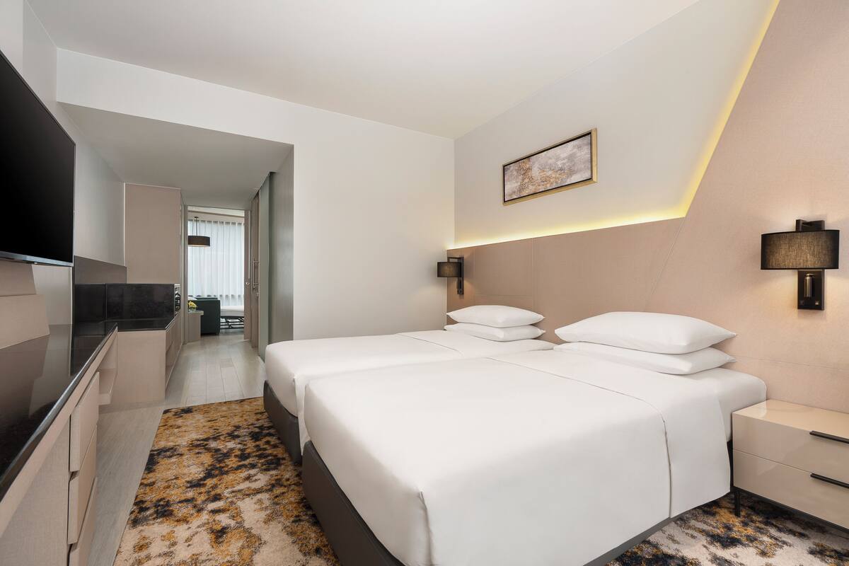 Habitación de hotel moderna con una cama grande, mesitas de noche, televisor de pantalla plana y vista al pasillo.