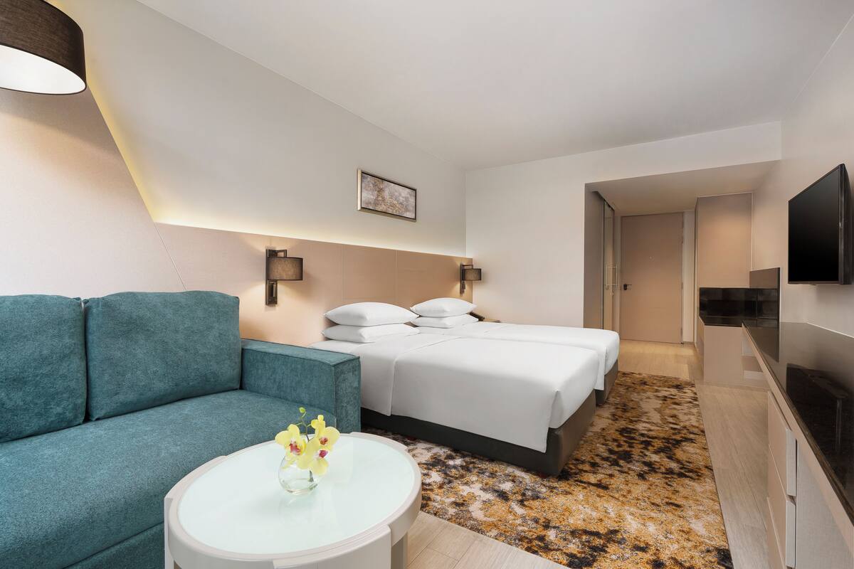 Habitación de hotel con sofá, cama, televisión y una pequeña mesa con flores.
