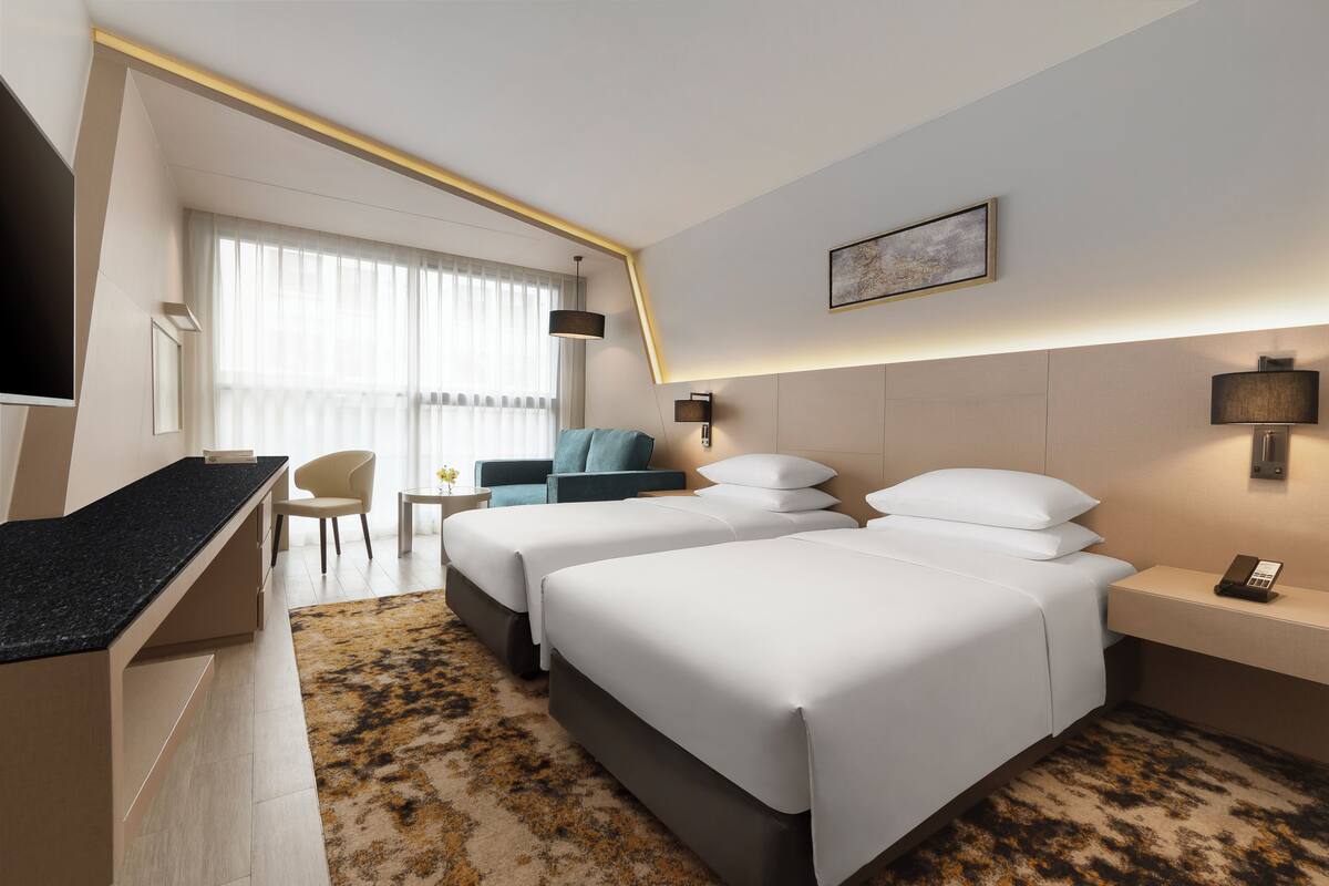 Habitación de hotel con dos camas, un escritorio, una silla, un televisor y una ventana con cortinas.