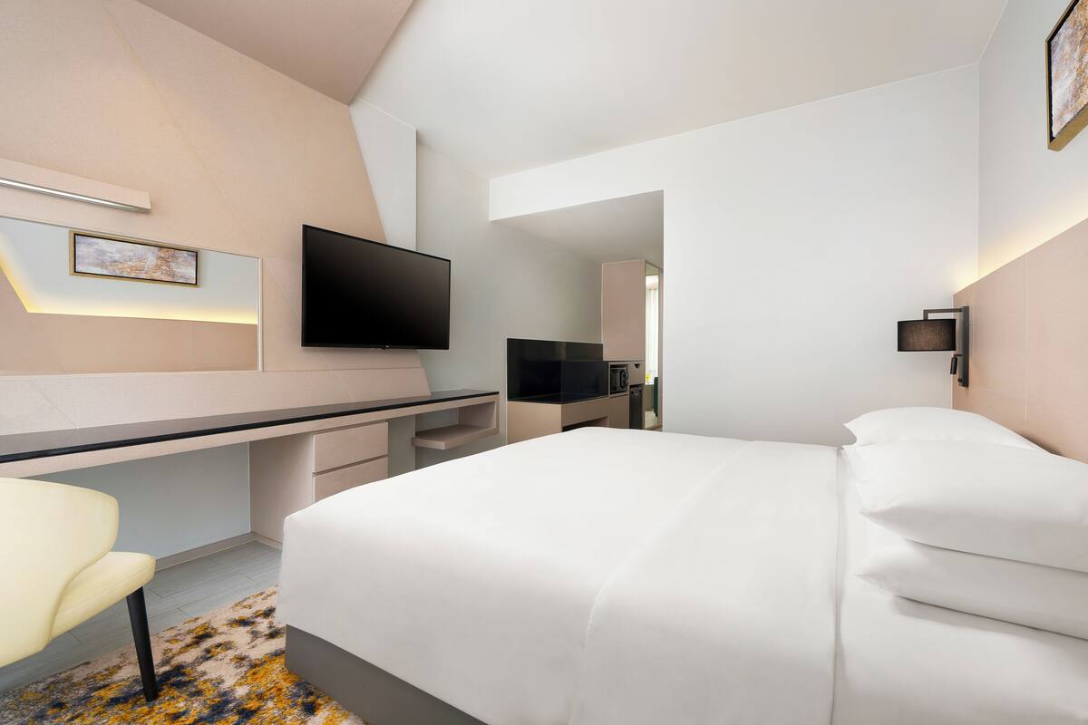 Una habitación de hotel moderna con cama, escritorio, silla, televisor de pantalla plana y una pequeña mesa.