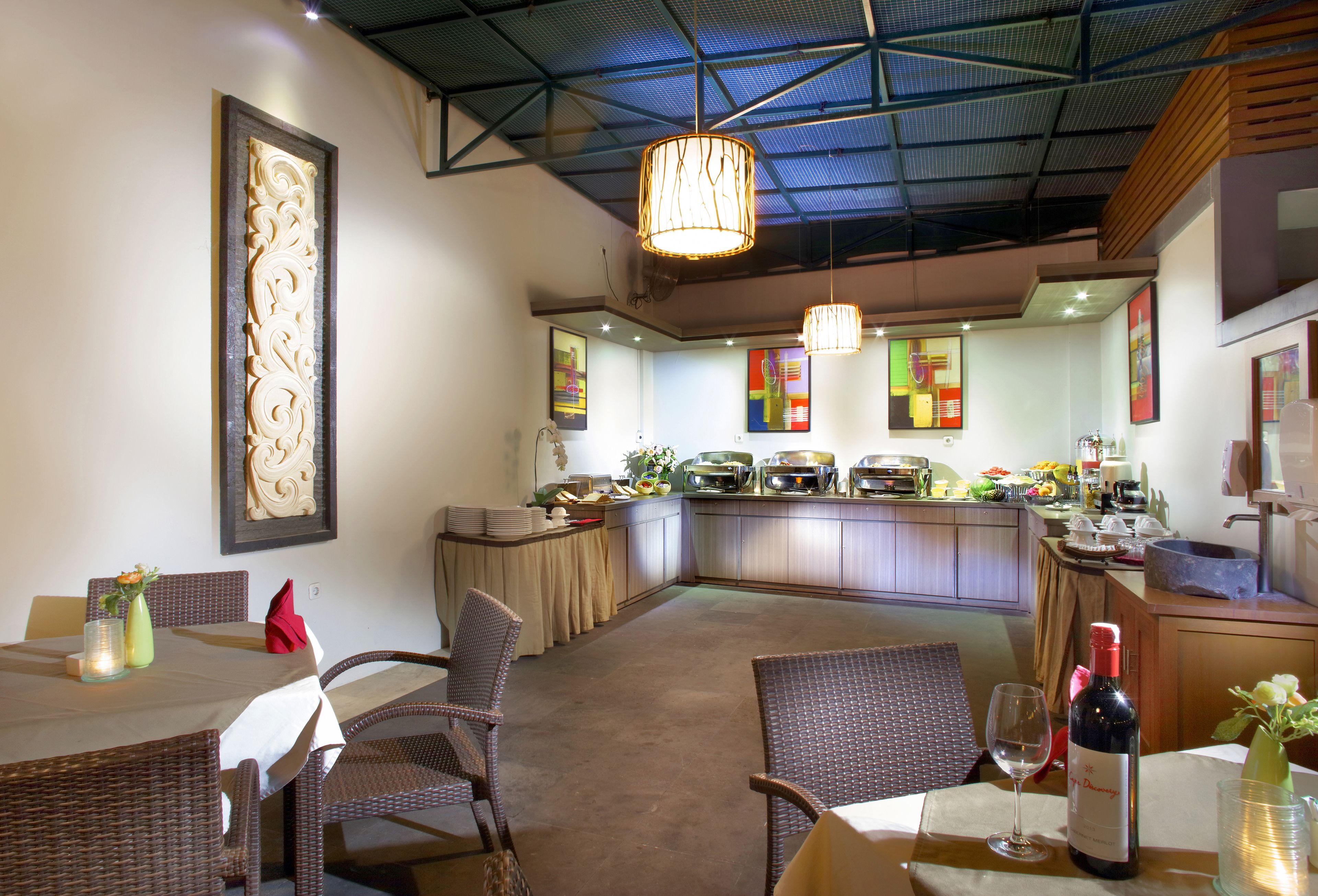 Un restaurante con barra central, mobiliario de mimbre y un techo con diseño geométrico.