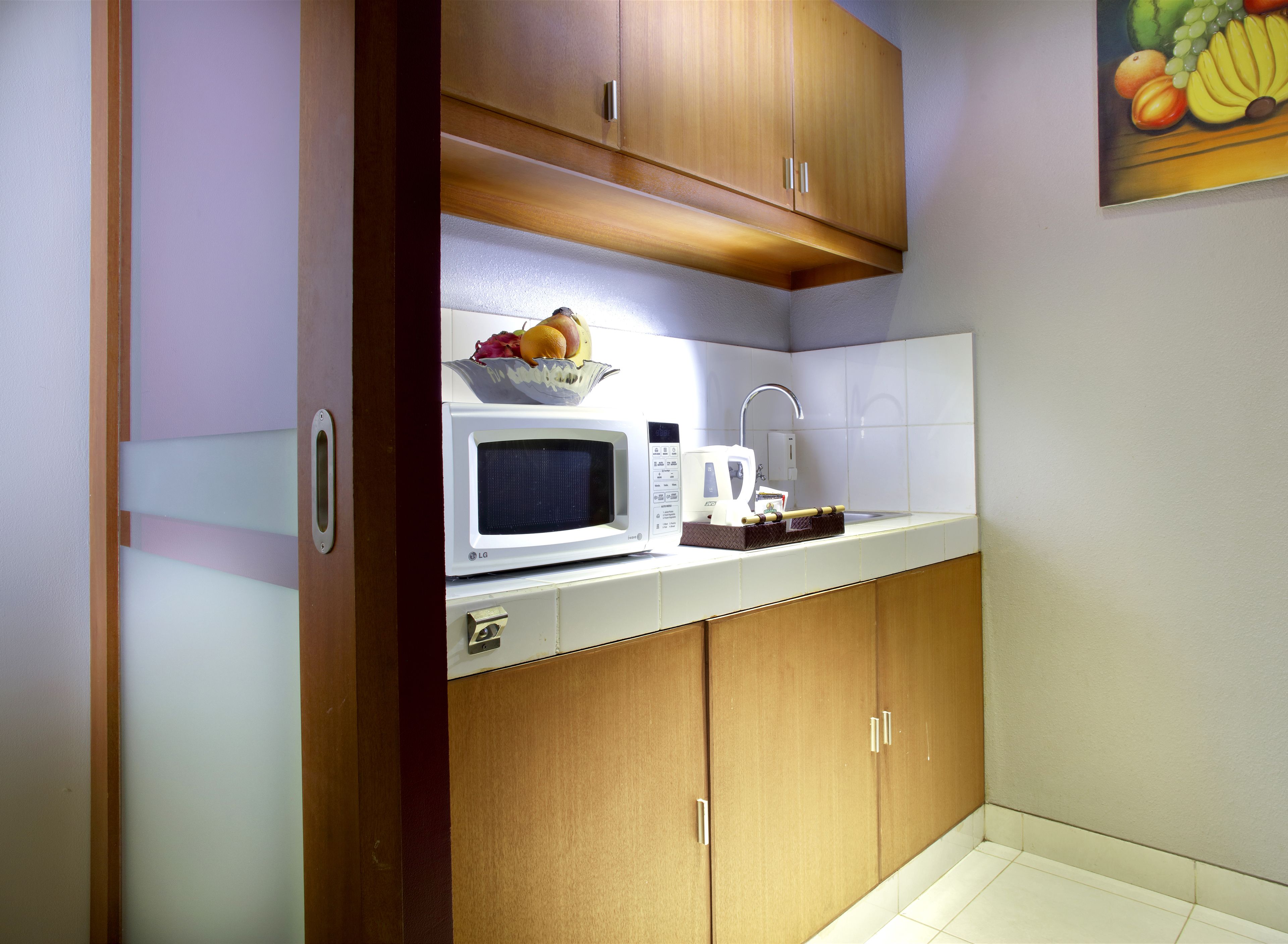A compact kitchen with a microwave, a fruit bowl, and a coffee maker on the counter.