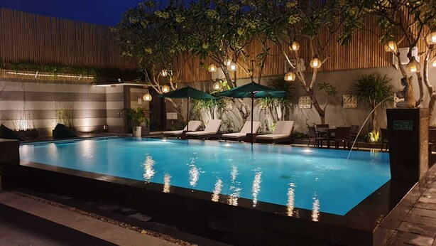 An outdoor swimming pool with lounge chairs and umbrellas, surrounded by trees and a bamboo fence. - The Banyumas Villa (Denpasar)