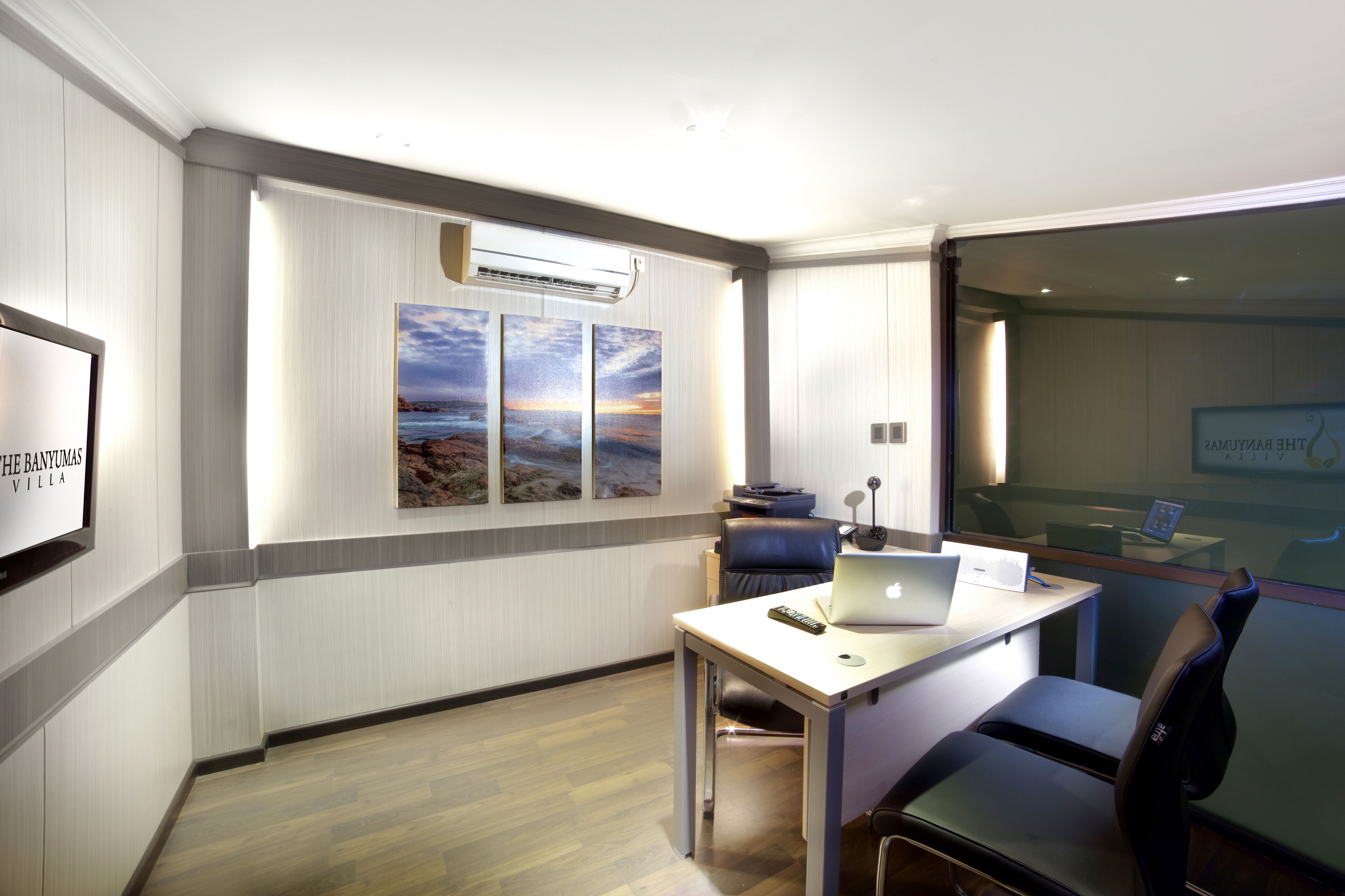 A modern hotel room with a desk, laptop, and a view of the sea through a glass wall.