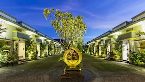A courtyard with a central sculpture, surrounded by buildings with balconies and palm trees. - The Banyumas Villa (Denpasar)