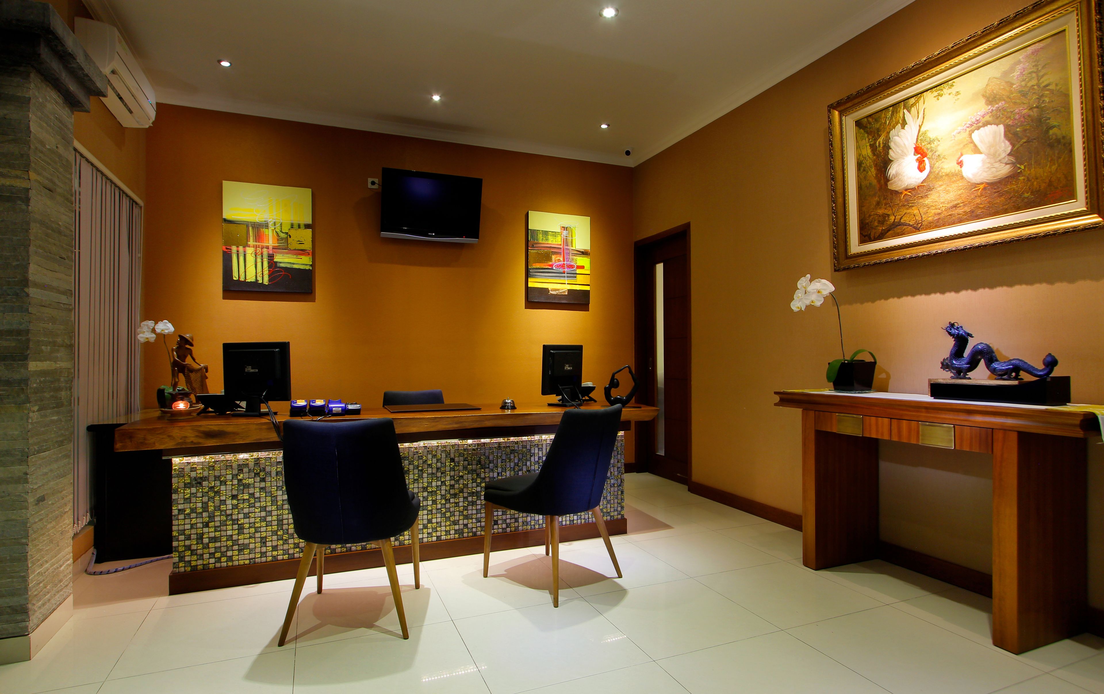 A reception area with a wooden desk, two chairs, a flat-screen TV, and artwork on the walls.