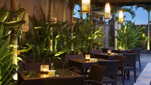 An outdoor dining area with wicker furniture and hanging lights, surrounded by tropical plants. - The Banyumas Villa (Denpasar)