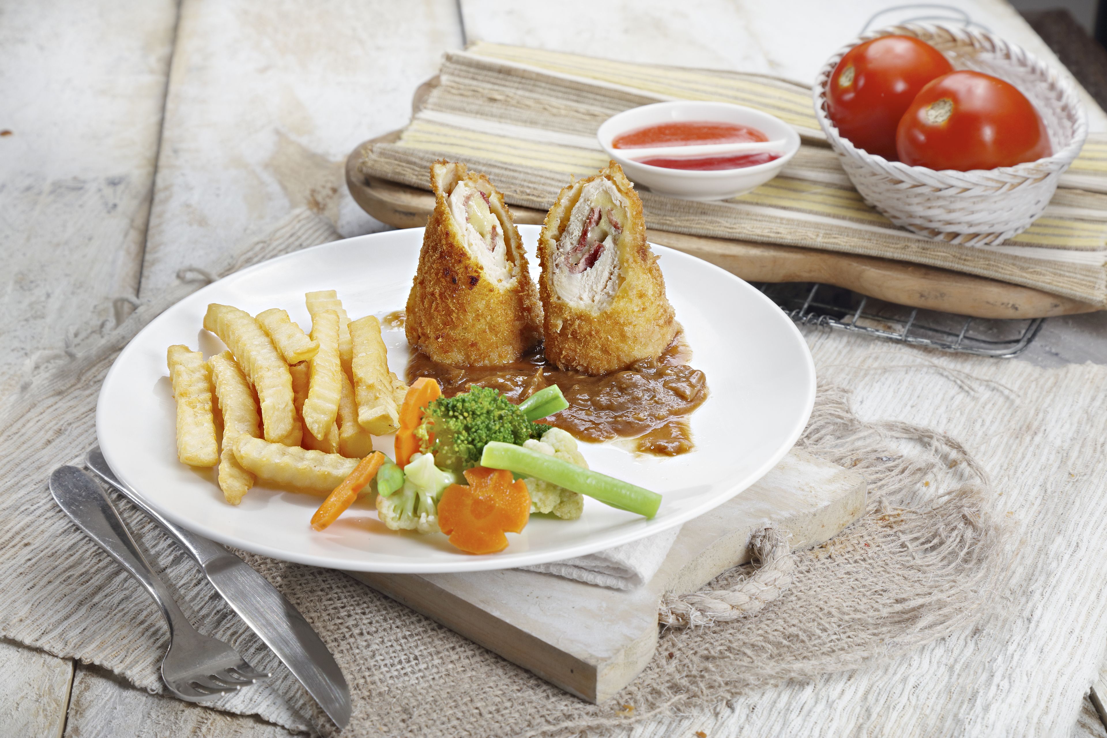 A plate of food with fries, vegetables, and a meat dish, served on a white plate with a fork and knife beside it.