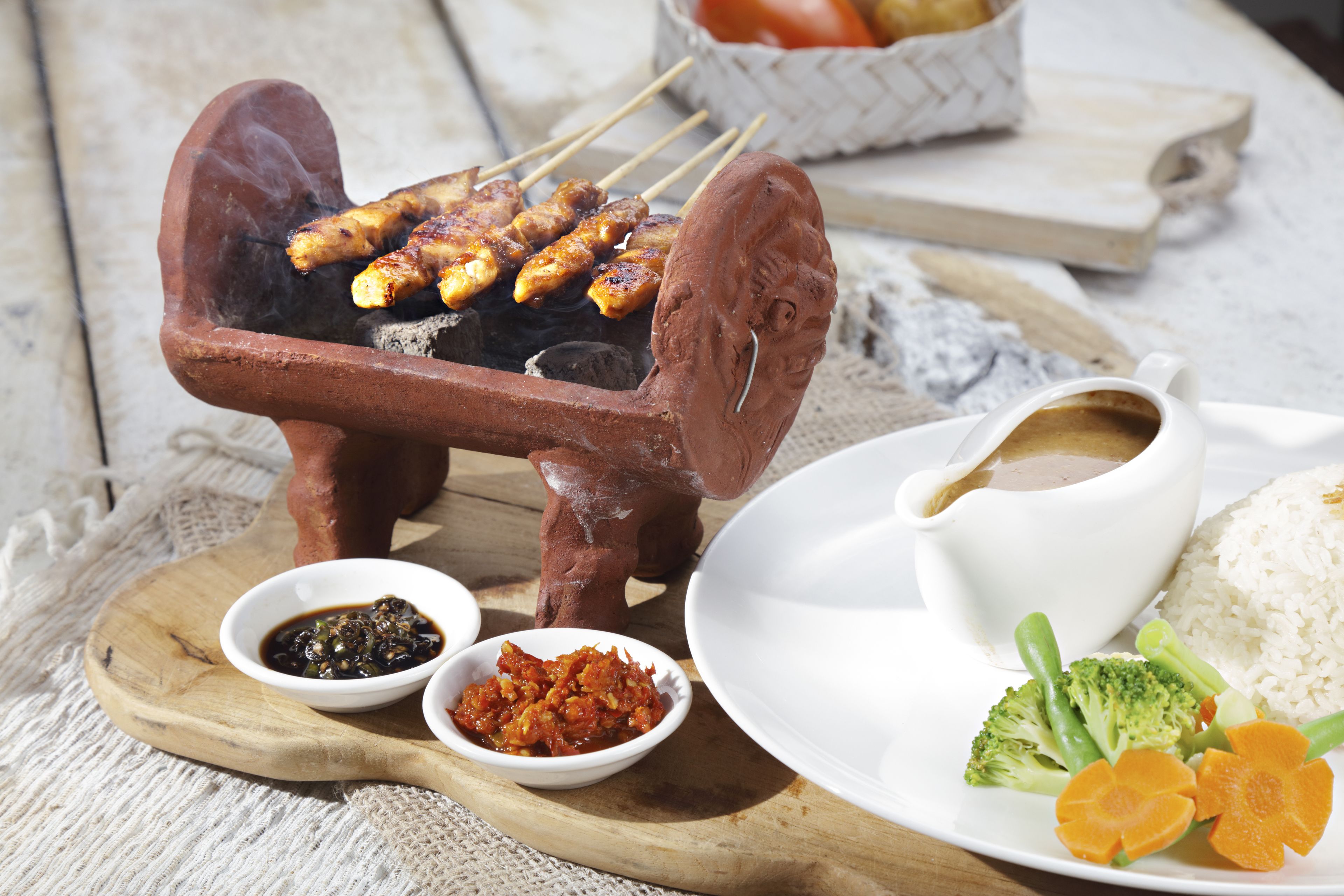 Una parrilla de arcilla tradicional con brochetas de carne a la parrilla, acompañadas de tazones de salsa, arroz y verduras.