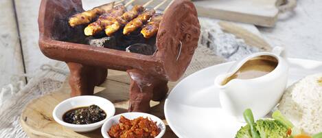 Una parrilla de arcilla tradicional con brochetas de carne a la parrilla, acompañadas de tazones de salsa, arroz y verduras.