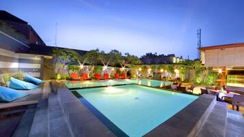 A rectangular swimming pool with a tiled deck, surrounded by red lounge chairs and a few tables and chairs.