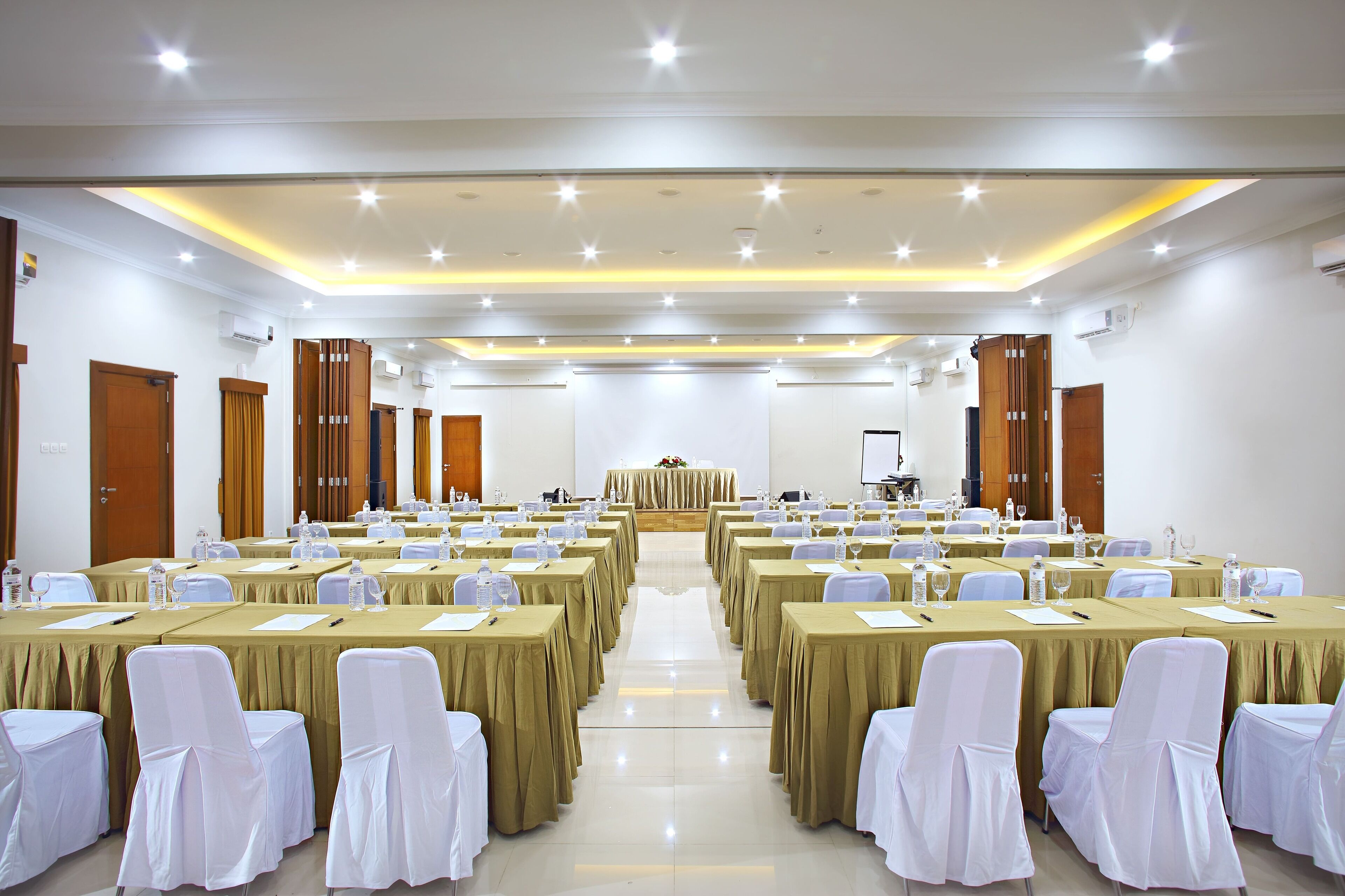 A conference room with rows of tables and chairs, a podium, and a projector screen.