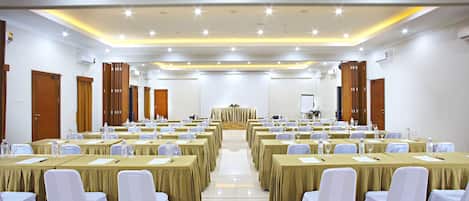 Uma sala de conferências com fileiras de mesas e cadeiras, um palanque e uma tela de projeção.