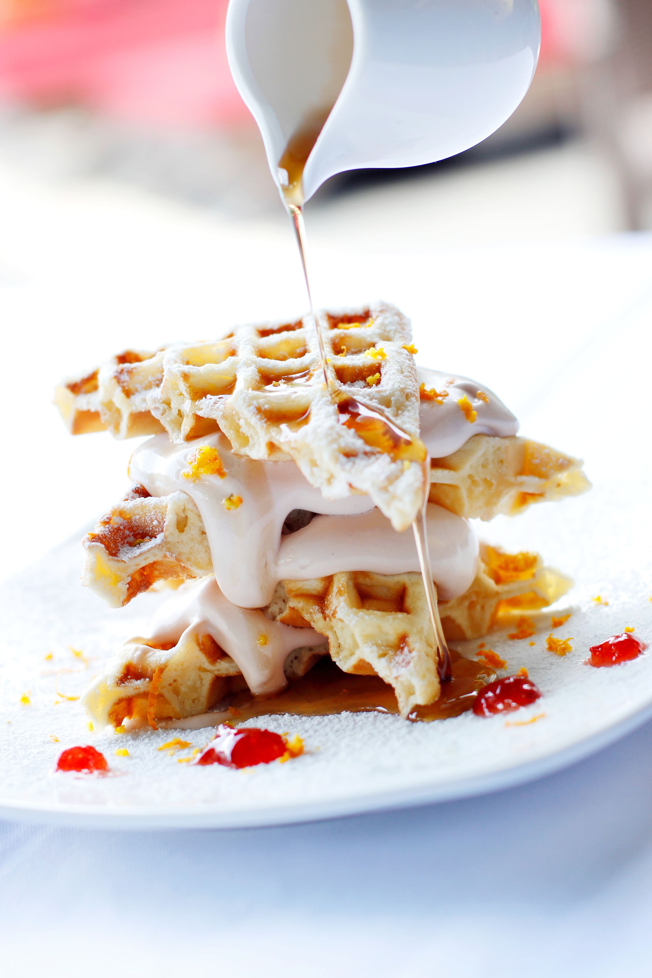A stack of waffles with syrup being poured over them.