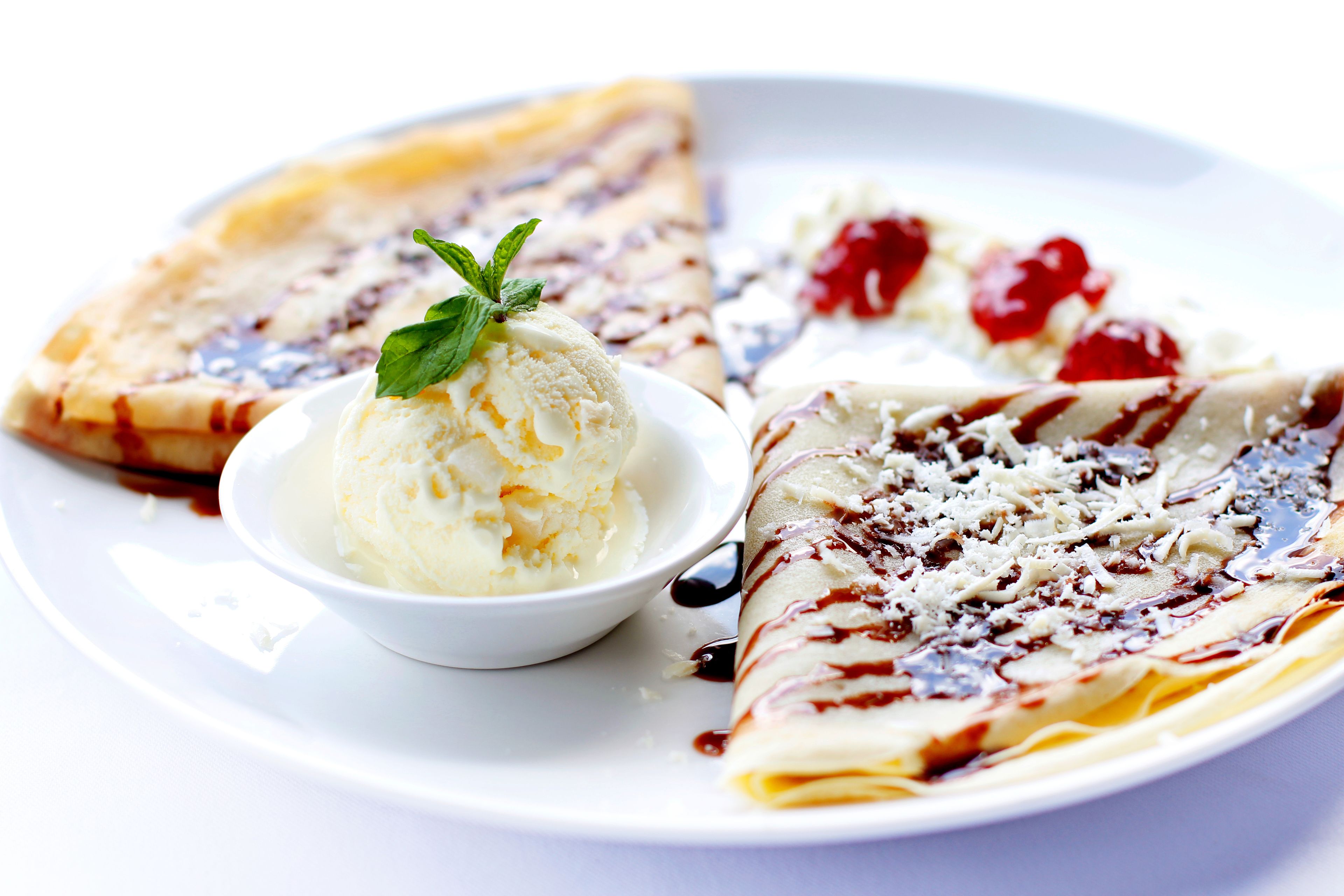 Un plato con tres crepes, uno con salsa de chocolate y fruta, otro con salsa de chocolate y crema batida, y un tercero con salsa de chocolate y una hoja de menta.