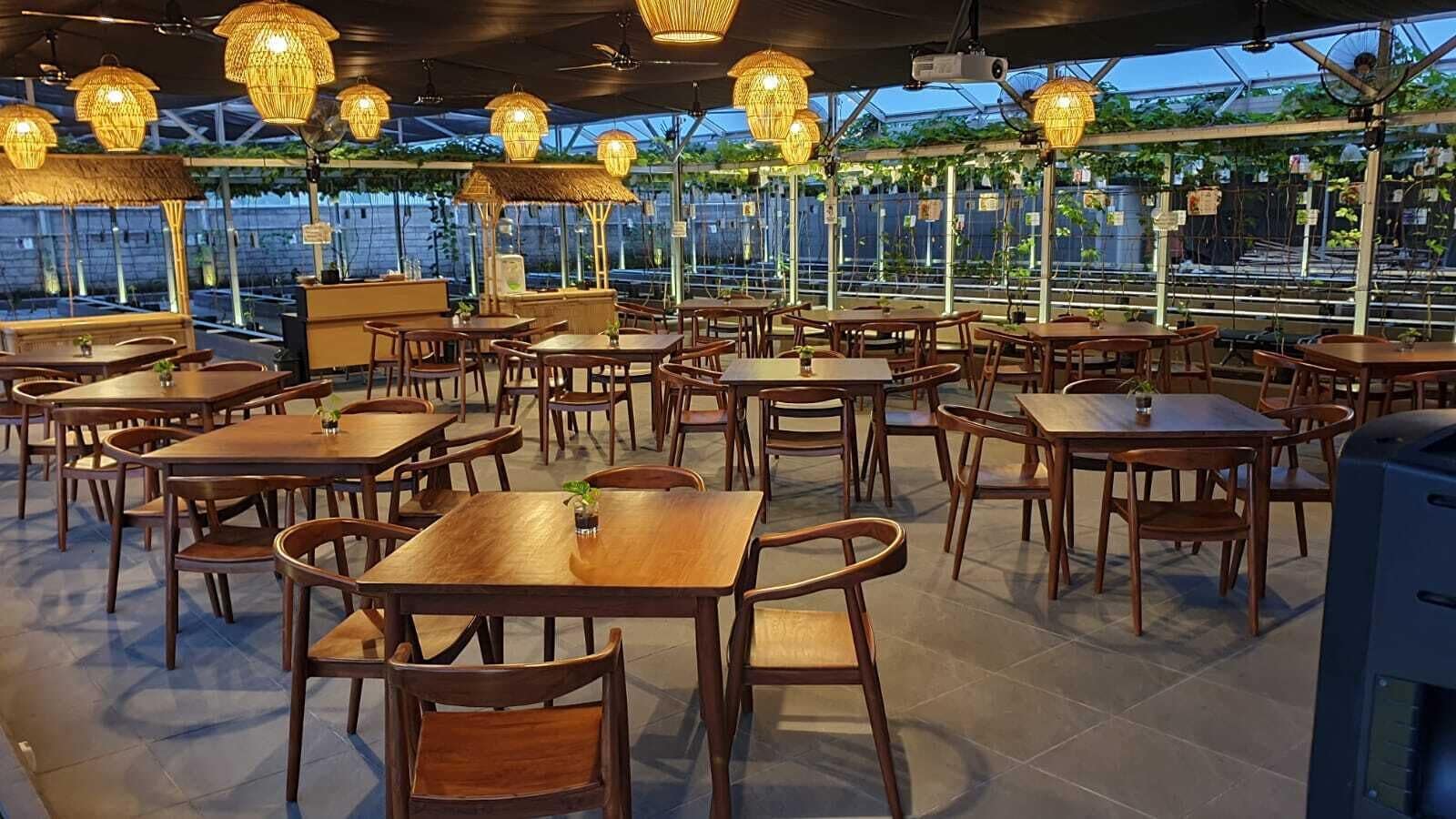 Un ristorante all'aperto con tavoli e sedie in legno, ombrelloni di paglia e vista su vegetazione e acqua.