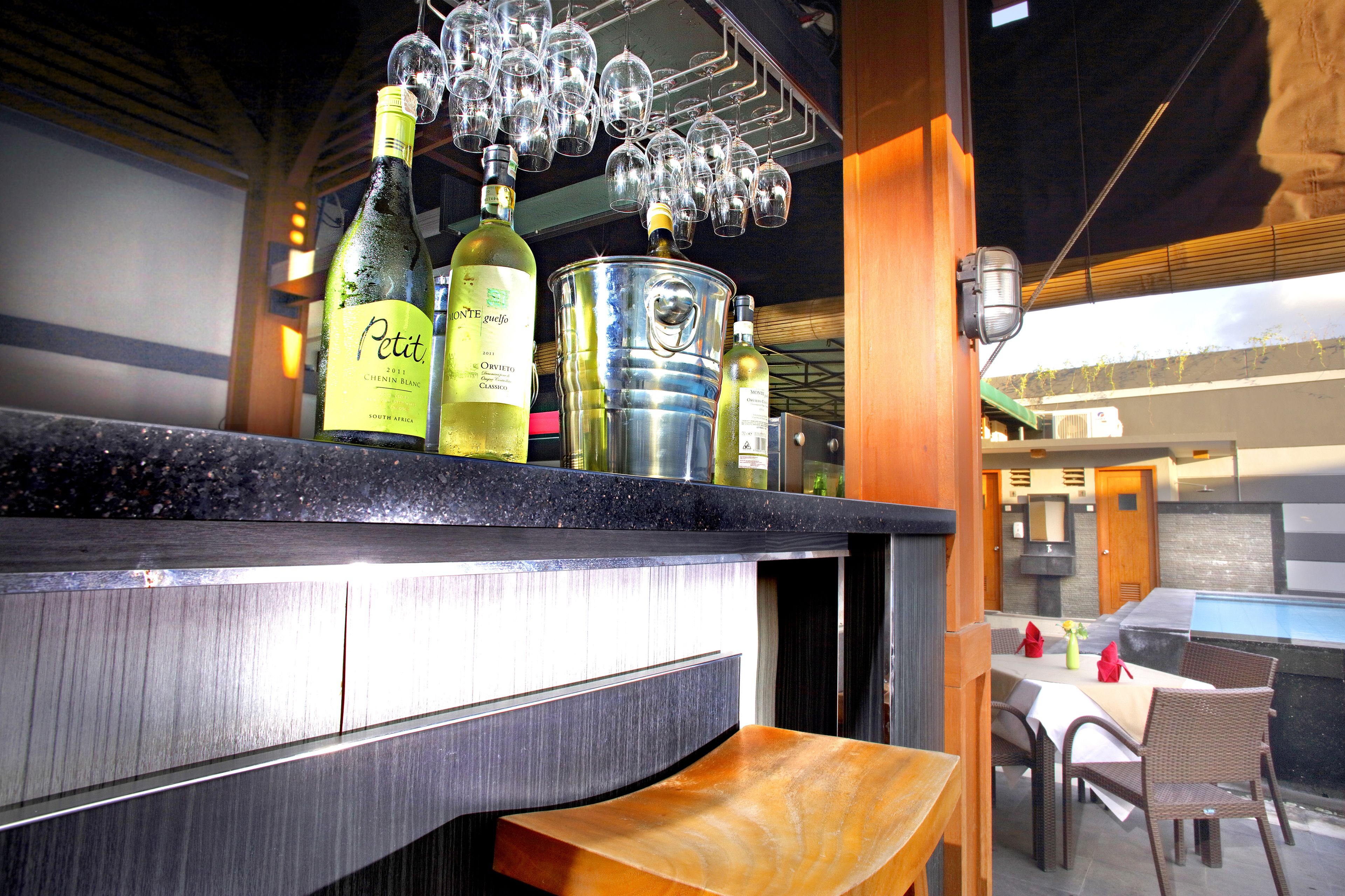 A bar area with bottles of wine, glasses hanging above, and a seating area with tables and chairs.
