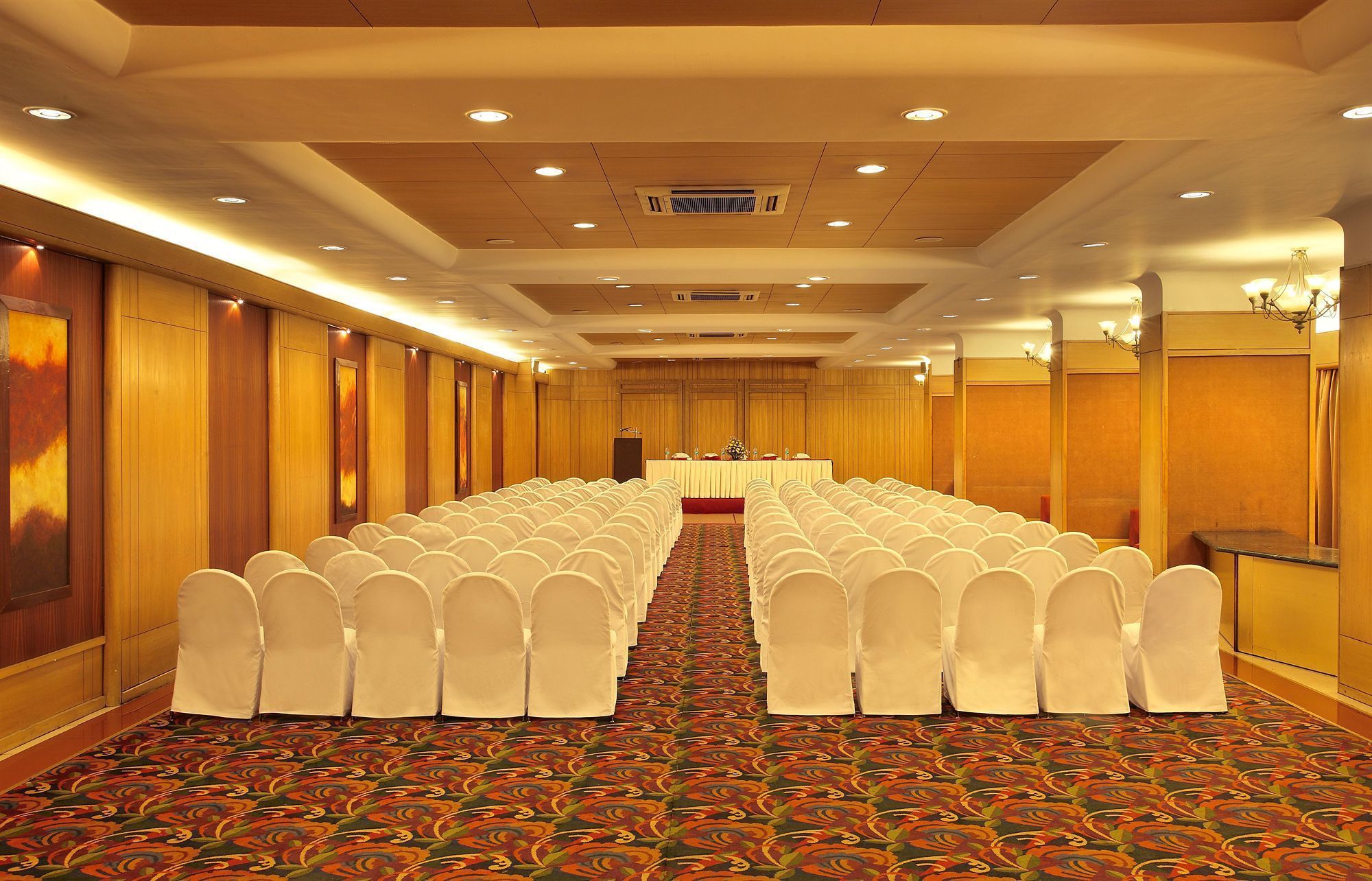 A conference room with rows of white chairs, a long table, and a carpeted floor.