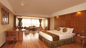 Habitación de hotel con una cama grande, un escritorio con silla, televisión y ventana con cortinas.