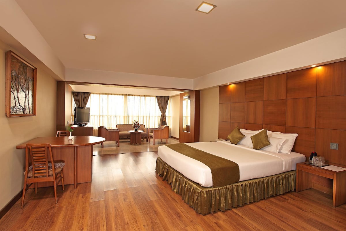 A hotel room with a large bed, a desk with a chair, a television, and a window with curtains.