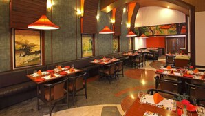 Un restaurante espacioso con varias mesas, lámparas colgantes naranjas y cuadros en las paredes.