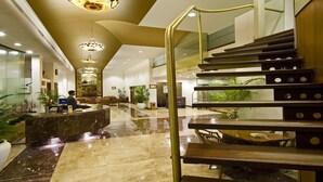Un vestíbulo amplio con piso de mármol, una mesa de recepción y una escalera de madera.