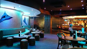 Zona de bar con taburetes y mesas, barra con un cantinero, y pared con un mural de ballena azul.