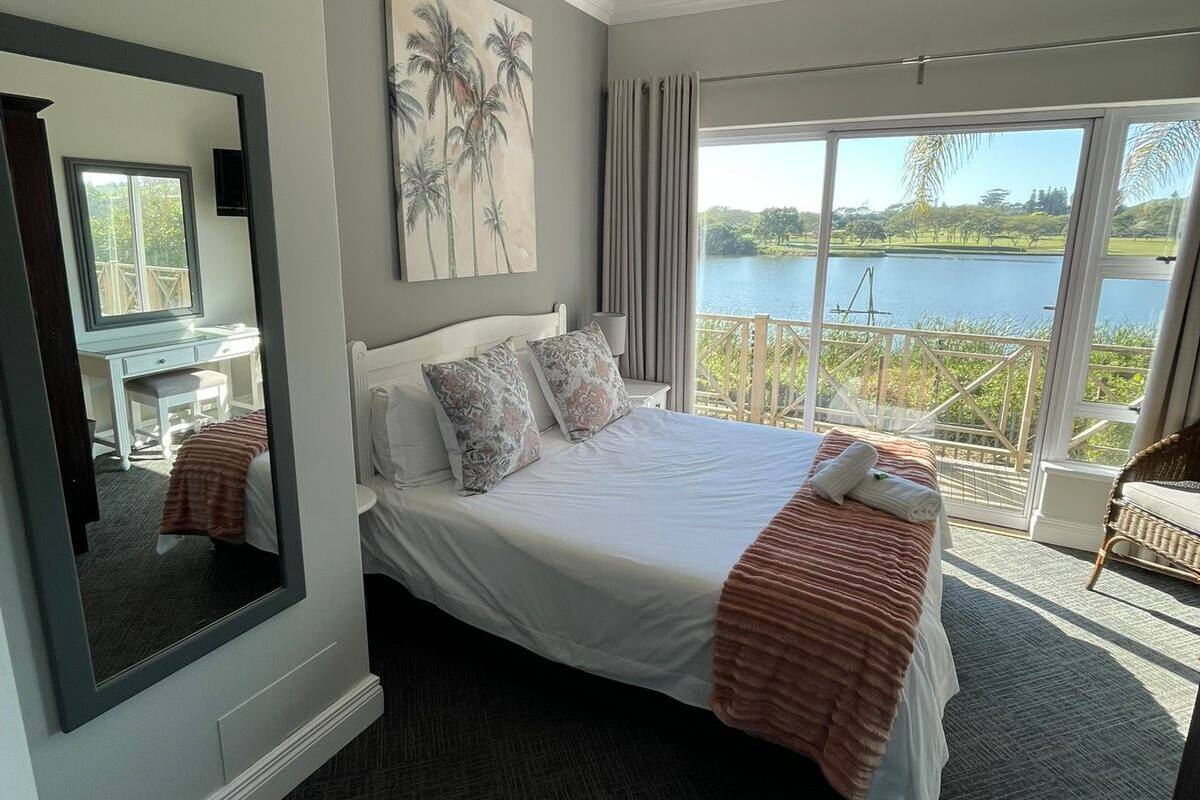 Une chambre avec un grand lit, un miroir, un tableau et une vue sur un lac.