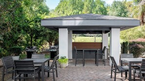 Une terrasse extérieure dotée d’un espace barbecue couvert, de sièges et de plantes en pot.