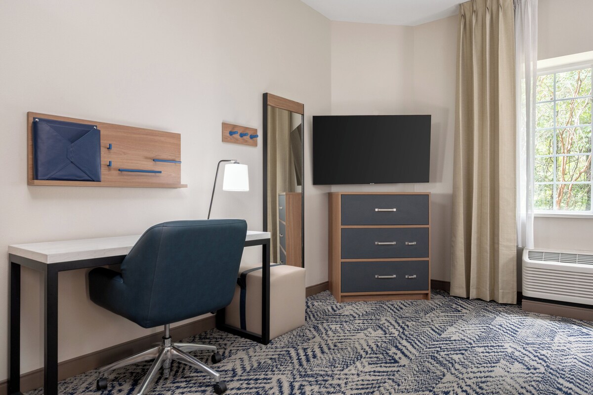 Ein Hotelzimmer mit Schreibtisch, Stuhl, Fernseher, Kleiderschrank und einem Fenster mit Vorhängen.