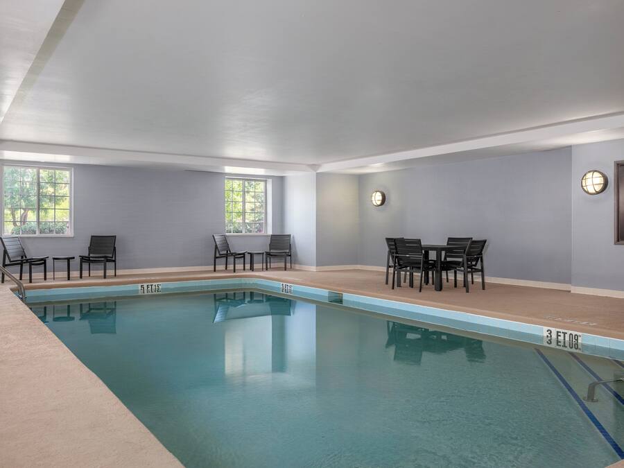 Una piscina interior con agua cristalina, rodeada de sillones y mesas.