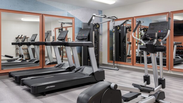 Une salle de sport équipée de tapis de course, de vélos elliptiques et de matériel de musculation.