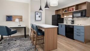 Une cuisine moderne dotée d’un îlot central, de tabourets de bar, d’une table à manger et d’un bureau.