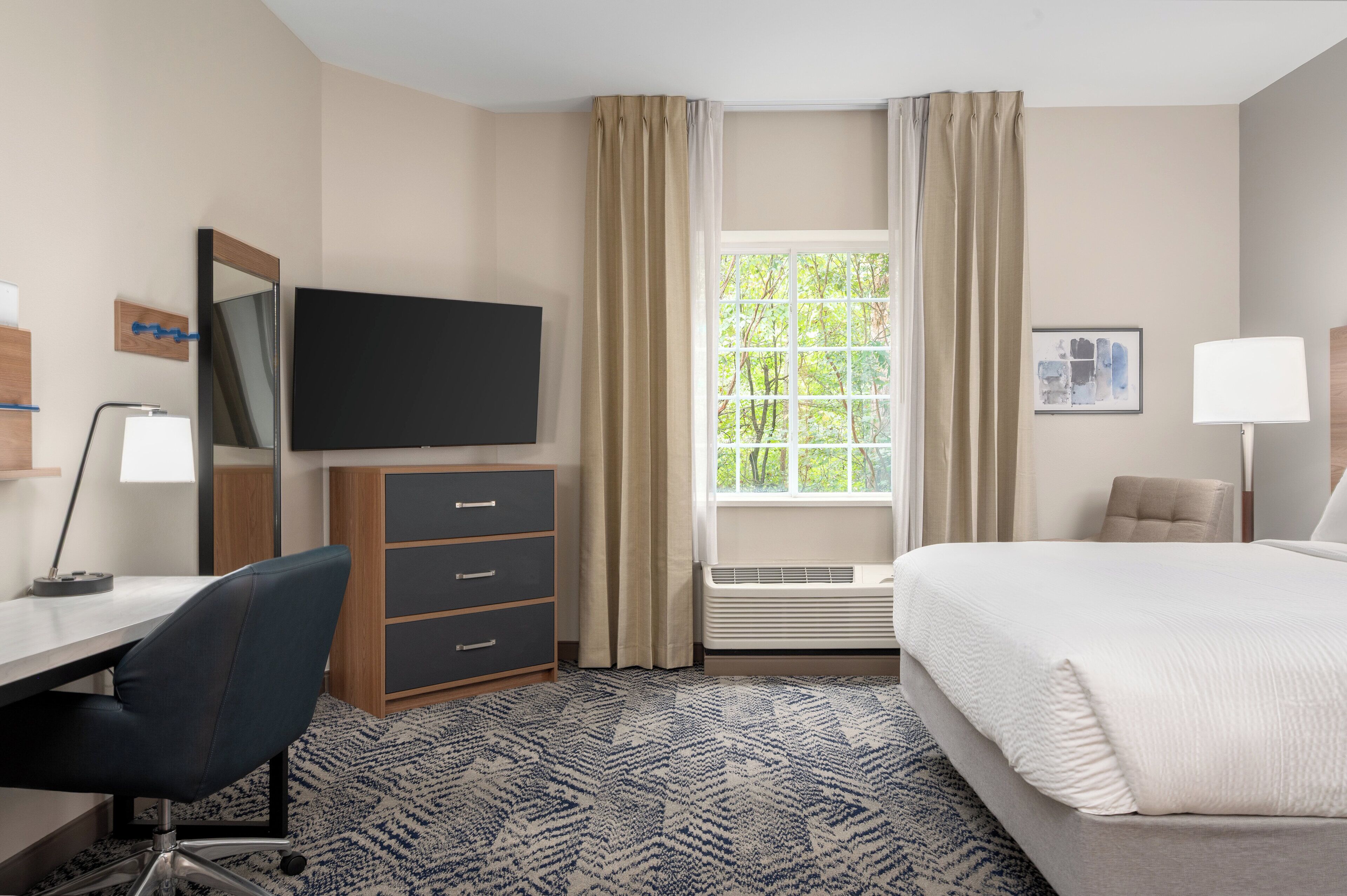 A hotel room with a bed, desk, chair, television, and a window with curtains.