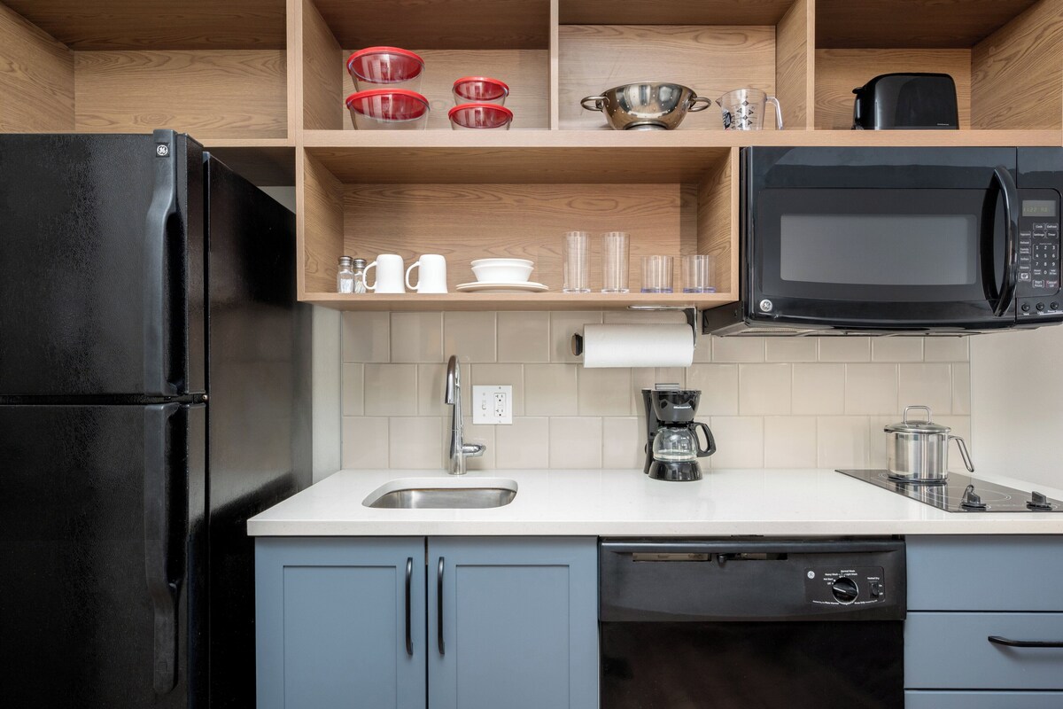 Eine moderne Küche mit einem schwarzen Kühlschrank, einer Mikrowelle, einer Kaffeemaschine und einem Geschirrspüler.