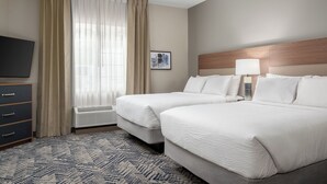 Une chambre d’hôtel avec deux lits, un téléviseur à écran plat, un bureau et une fenêtre avec des rideaux.