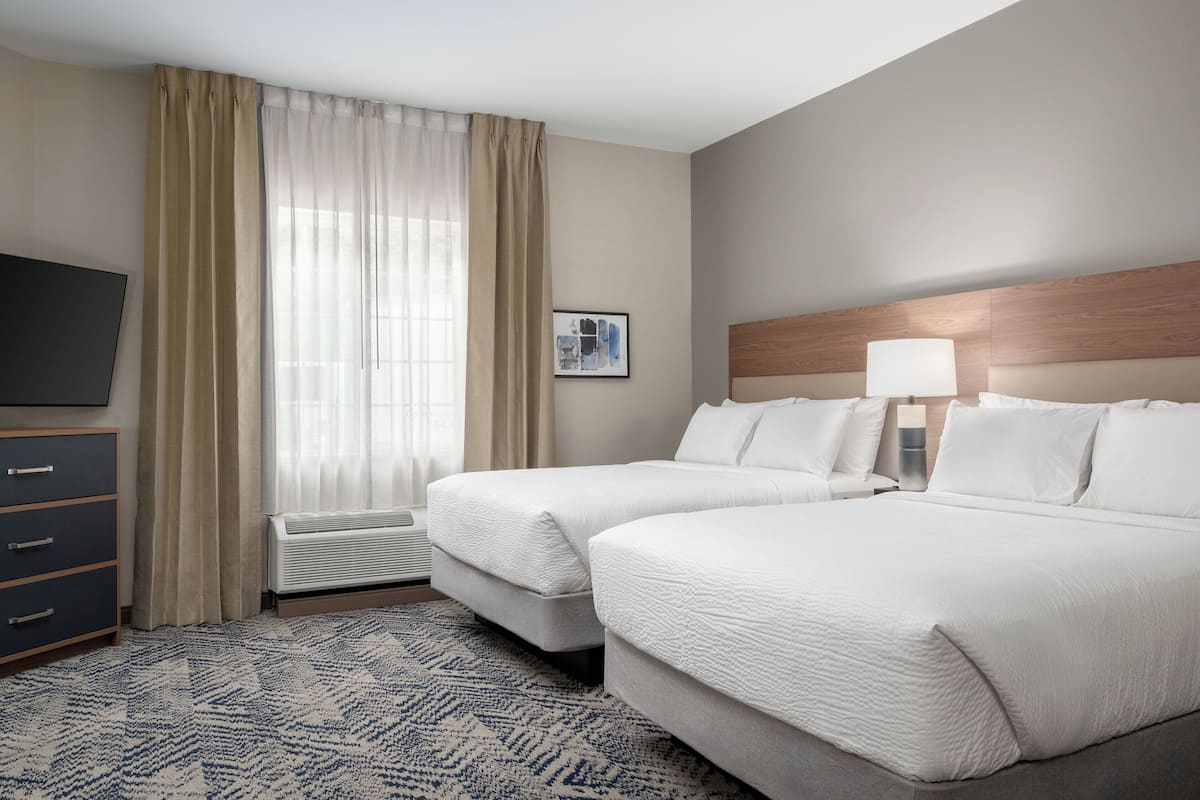 Une chambre d’hôtel avec deux lits, un téléviseur à écran plat, un bureau et une fenêtre avec des rideaux.