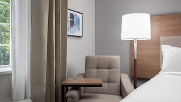 A hotel room with a bed, a chair, a small table, a lamp, and a window with curtains.