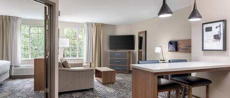 A hotel room with a bed, a sofa, a desk with two chairs, a TV, and a large window with curtains.