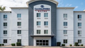 Un hôtel moderne, reconnaissable à son panneau bien visible indiquant « CANDLEWOOD SUITES », qui se distingue par sa façade symétrique, avec des fenêtres régulièrement espacées et une entrée centrale.