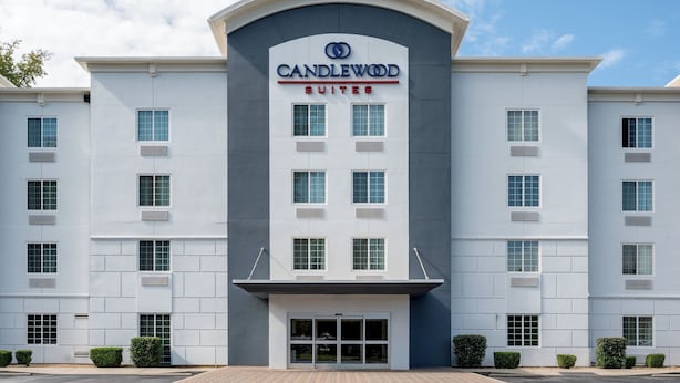 A modern hotel with a prominent "CANDLEWOOD SUITES" sign, featuring a symmetrical facade with evenly spaced windows and a central entrance.
