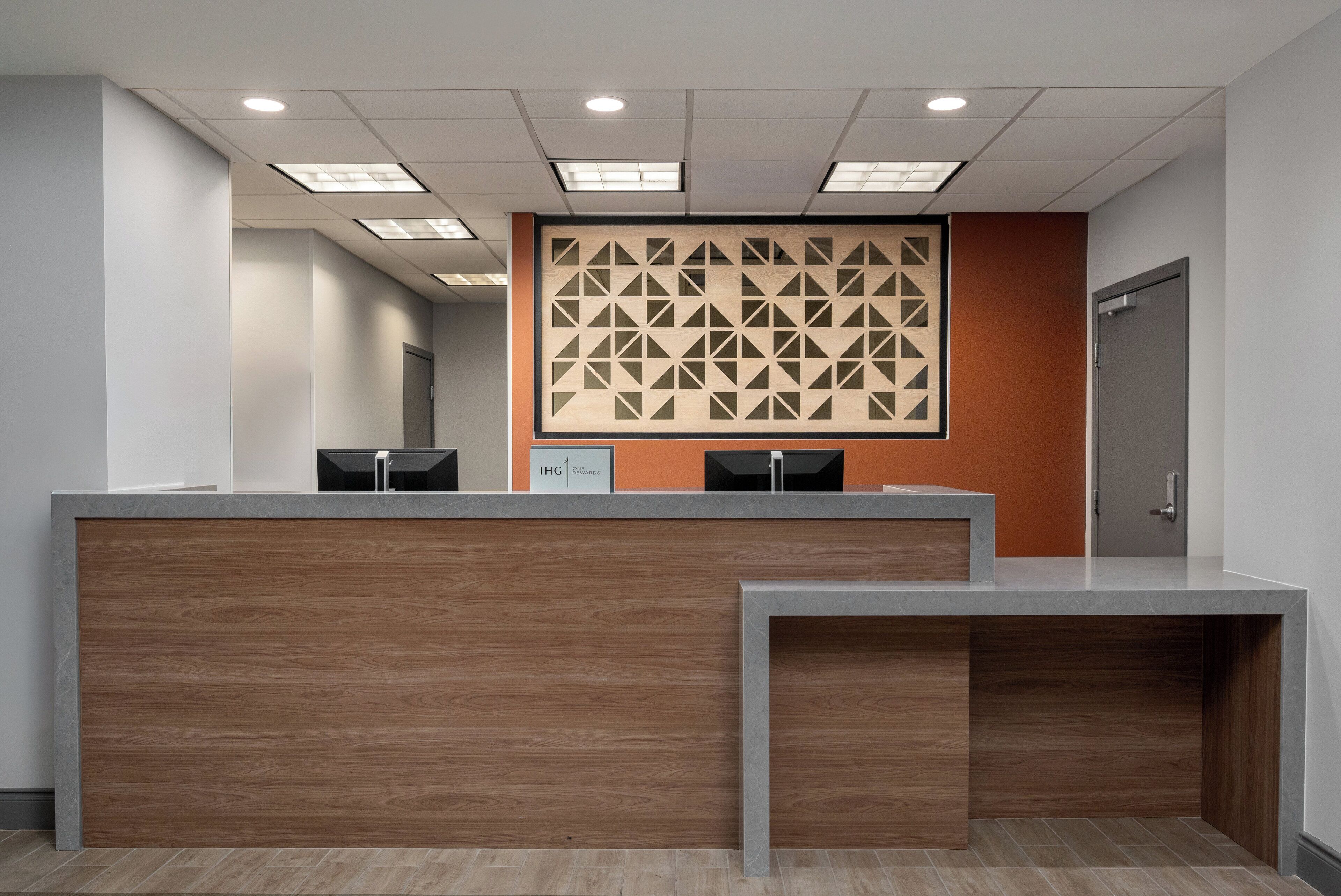 A reception area with a wooden reception desk, a patterned wall, and a door to the right.