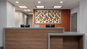 A reception area with a wooden reception desk, a patterned wall, and a door to the right.