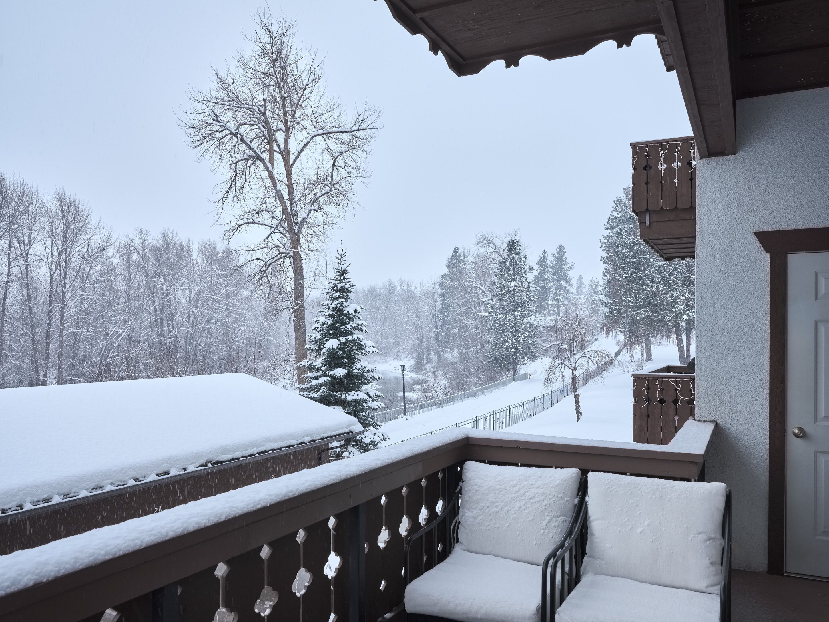 A balcony with a view of a snow-covered landscape, including trees and a fence.