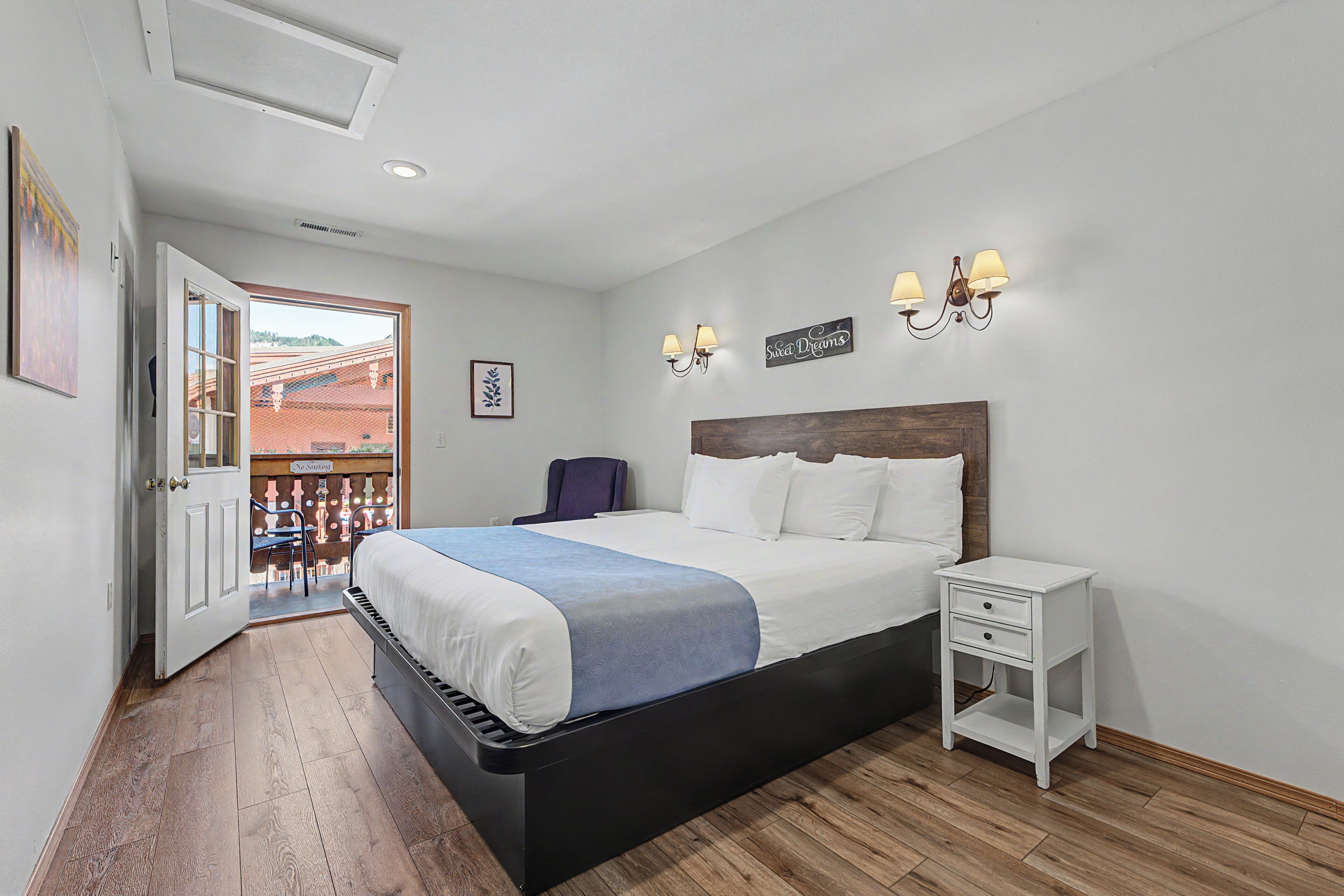 Un dormitorio con cama, mesita de noche, lámparas de pared y puerta que da a un espacio exterior.