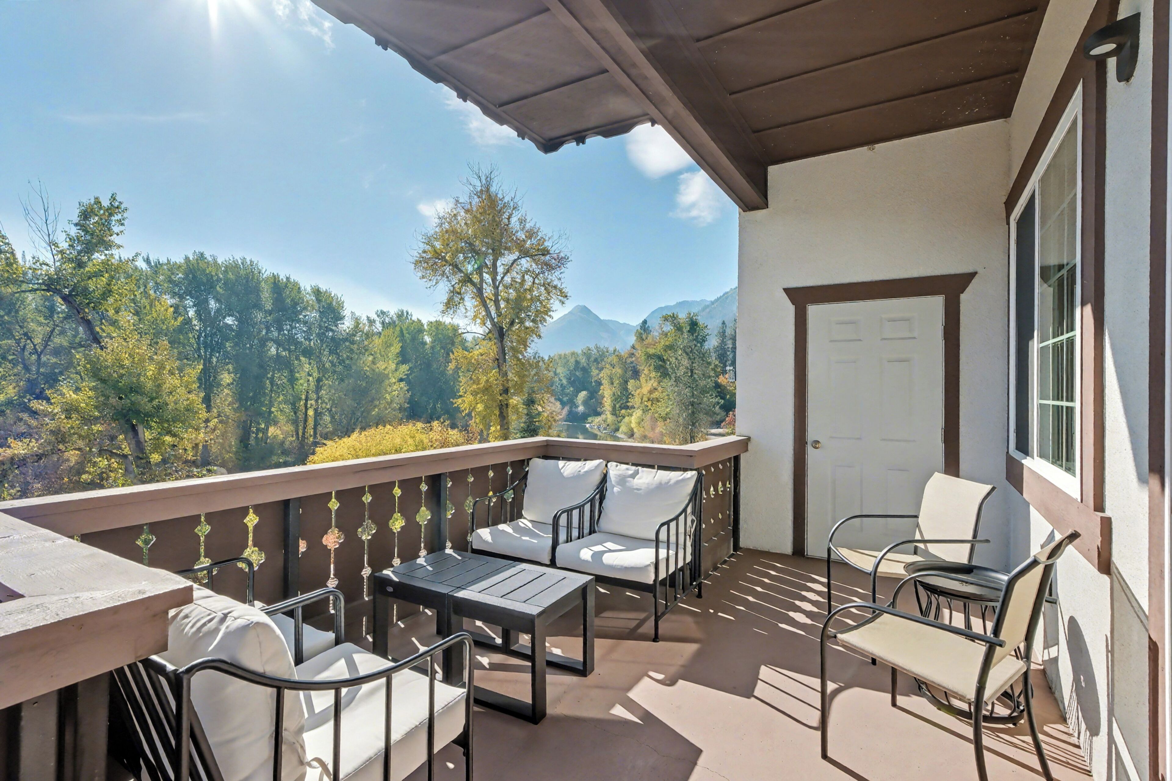 Un balcon avec des meubles d’extérieur, une vue sur les arbres et les montagnes, et une porte.